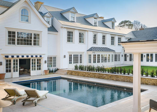 Large white house with a pool and lounge chairs on a sunny day