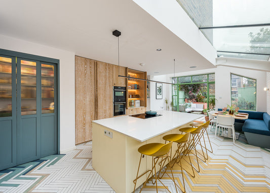 Modern kitchen with white island, yellow stools, and a view of the living room.